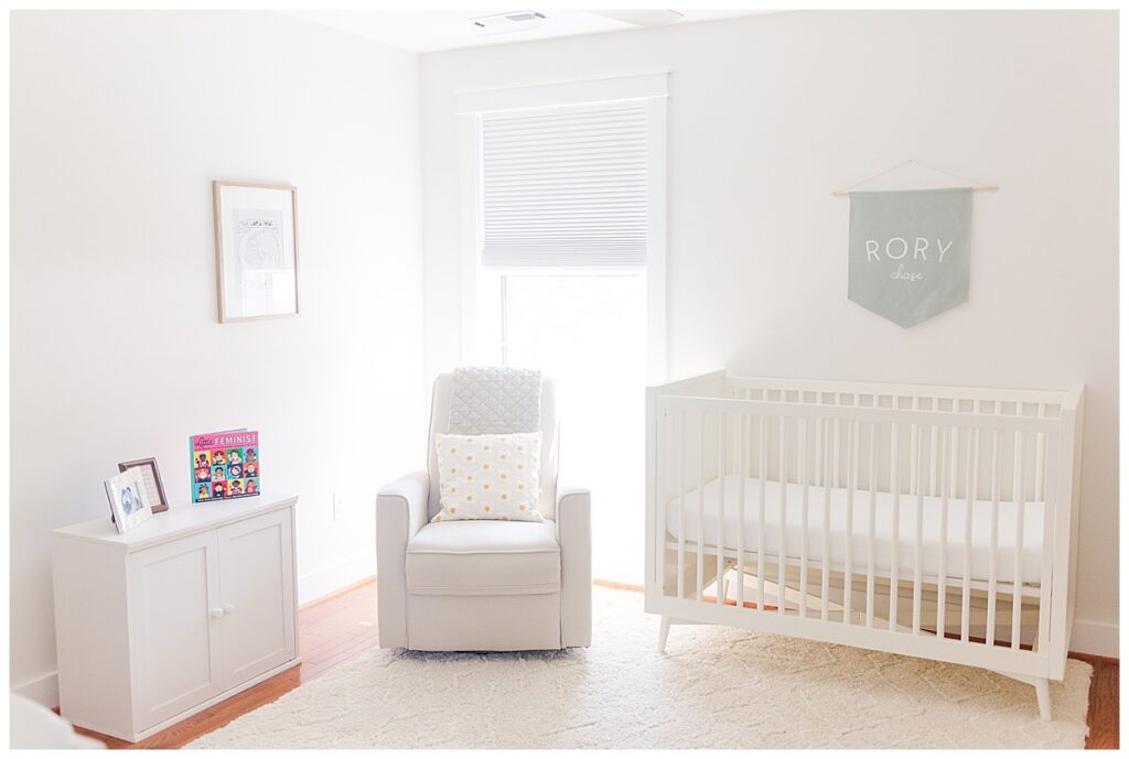 A white newborn nursery with books, comfy chair and a crib.