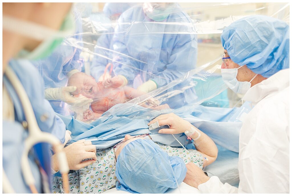 Parents see their newborn baby through a clear drape during their positive c-section birth.