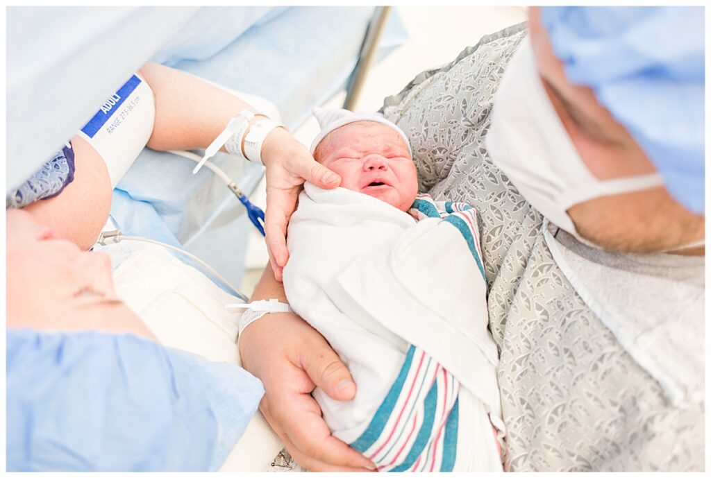 Two parents embracing their new baby in the operating room after a c-section.