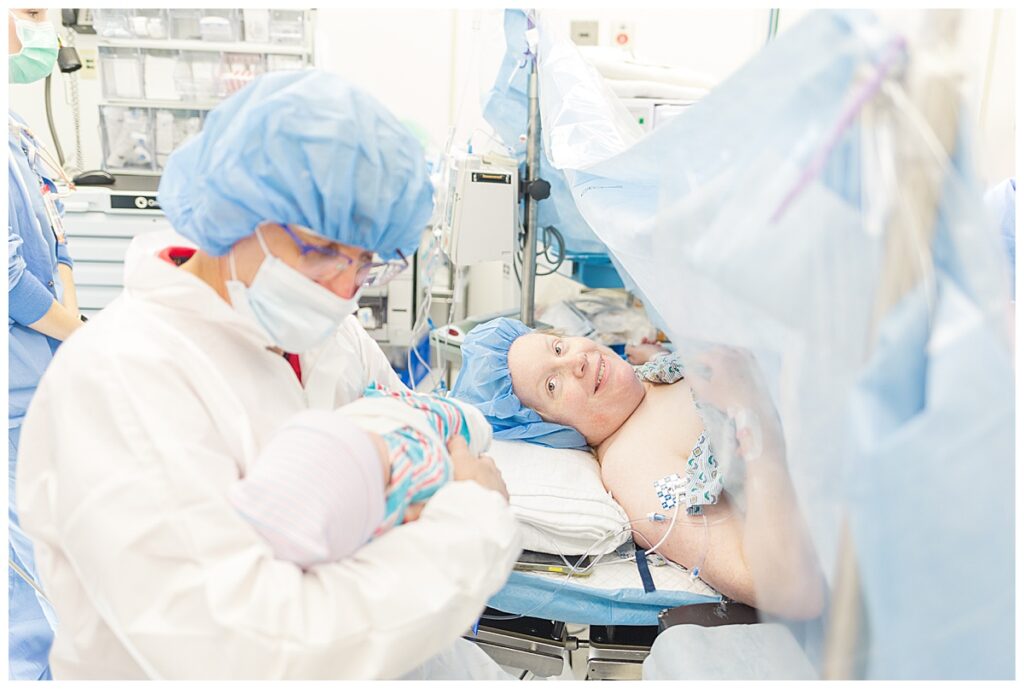 A mom lays on the operating table looking lovingly at her husband holding their newborn baby after a positive scheduled c-section.